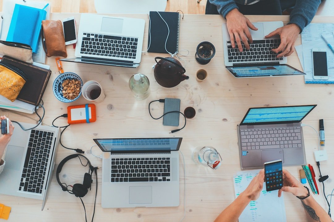 Top view of desk with multiple laptops where a team is collaborating thanks to the benefits of professional services automation